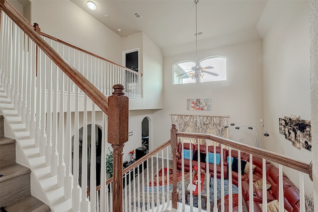 stairs with hardwood / wood-style floors, a towering ceiling, and ceiling fan