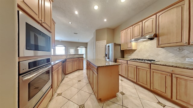 kitchen with stainless steel appliances, sink, a center island, a textured ceiling, and tasteful backsplash