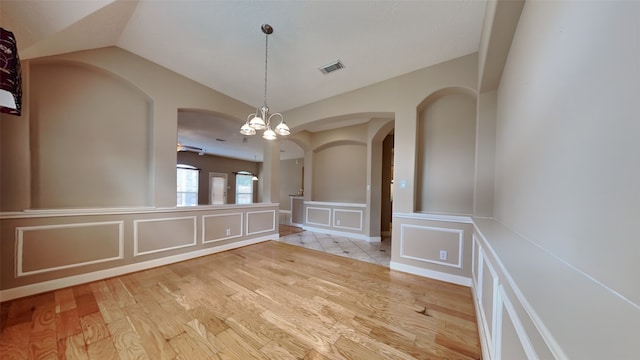 unfurnished dining area with lofted ceiling, ceiling fan with notable chandelier, and light wood-type flooring