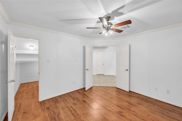 unfurnished bedroom with a spacious closet, ornamental molding, light wood-type flooring, and ceiling fan