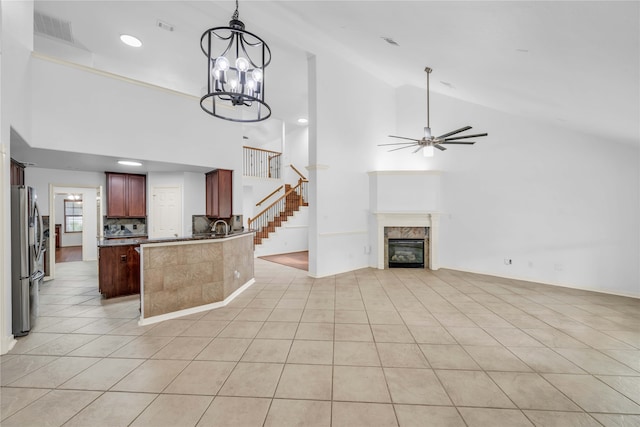 unfurnished living room with high vaulted ceiling, a premium fireplace, light tile patterned floors, and ceiling fan with notable chandelier