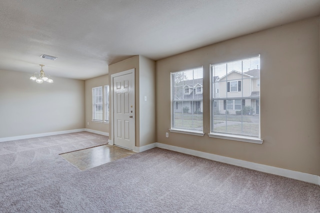 spare room featuring a textured ceiling, light carpet, and a notable chandelier