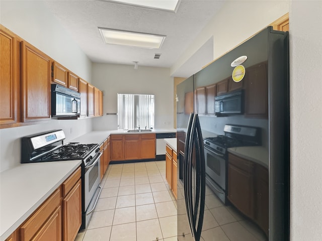 kitchen featuring a textured ceiling, black appliances, sink, and light tile patterned floors