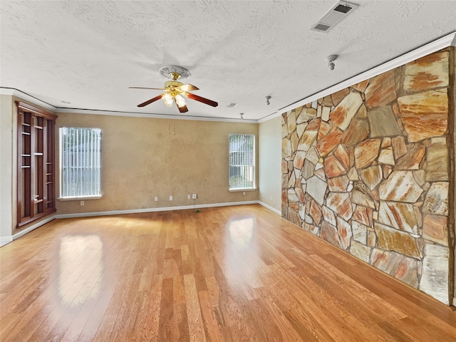 empty room featuring ceiling fan, a textured ceiling, light hardwood / wood-style flooring, and ornamental molding