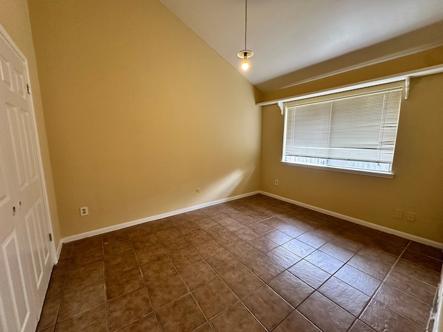 spare room featuring vaulted ceiling and dark tile patterned flooring