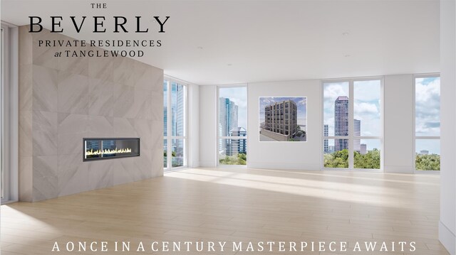 unfurnished living room featuring light hardwood / wood-style floors, a wall of windows, a healthy amount of sunlight, and a tiled fireplace