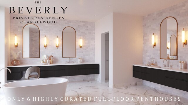 full bath featuring two vanities, a sink, marble finish floor, a freestanding bath, and tile walls