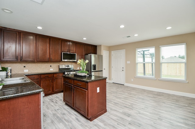 kitchen with backsplash, a center island, appliances with stainless steel finishes, and light hardwood / wood-style floors