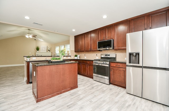 kitchen featuring lofted ceiling, tasteful backsplash, a center island with sink, appliances with stainless steel finishes, and light hardwood / wood-style flooring