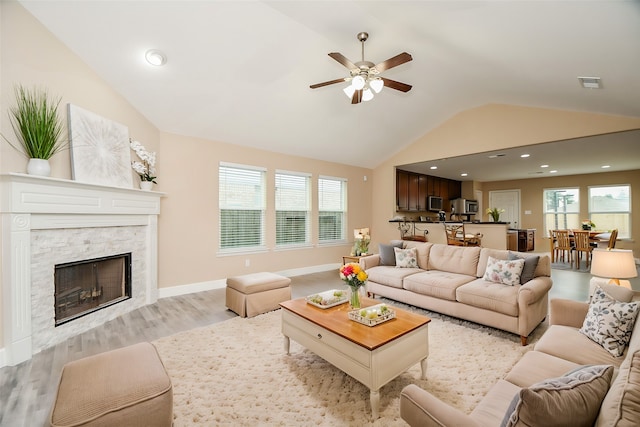 living room featuring lofted ceiling, light hardwood / wood-style flooring, a stone fireplace, and ceiling fan