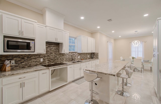 kitchen featuring hanging light fixtures, a kitchen breakfast bar, stainless steel microwave, black electric cooktop, and crown molding