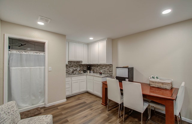 kitchen with decorative backsplash, white cabinets, hardwood / wood-style flooring, and light stone counters