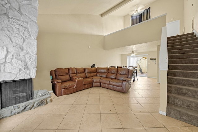 living room featuring ceiling fan, a stone fireplace, beamed ceiling, and light tile patterned flooring