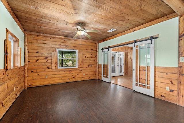 empty room featuring ceiling fan, dark hardwood / wood-style flooring, a barn door, wooden ceiling, and wooden walls