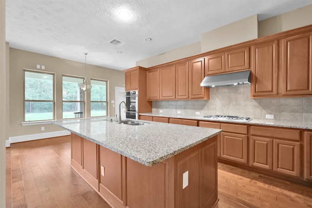 kitchen featuring sink, light stone counters, backsplash, a kitchen island with sink, and light hardwood / wood-style flooring