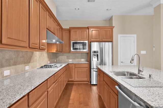 kitchen featuring light stone counters, appliances with stainless steel finishes, exhaust hood, sink, and hardwood / wood-style floors