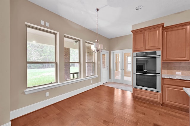 kitchen featuring an inviting chandelier, backsplash, hanging light fixtures, double oven, and light wood-type flooring