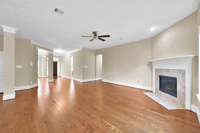 unfurnished living room with ornate columns, hardwood / wood-style floors, a tile fireplace, ornamental molding, and ceiling fan