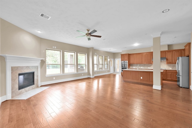 unfurnished living room featuring a fireplace, ceiling fan, sink, and light wood-type flooring