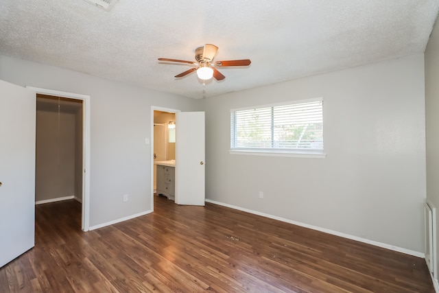 unfurnished bedroom with a spacious closet, a textured ceiling, dark hardwood / wood-style flooring, a closet, and ceiling fan