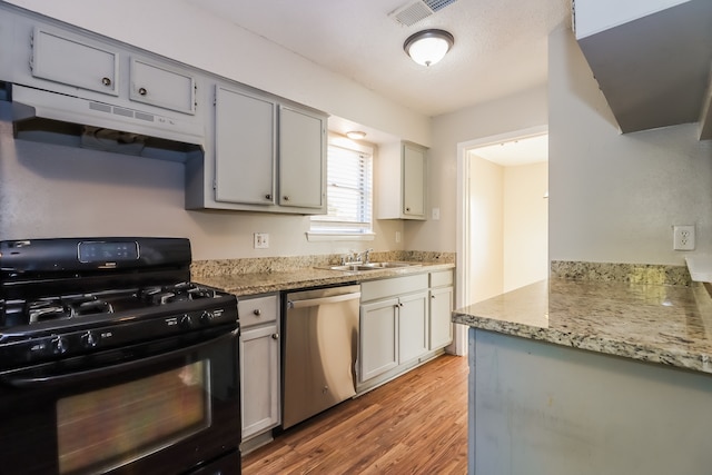 kitchen with black range with gas stovetop, light stone countertops, sink, stainless steel dishwasher, and light hardwood / wood-style flooring