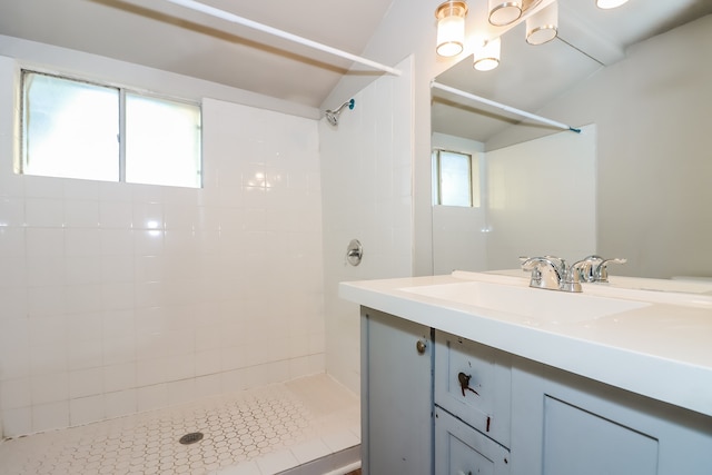 bathroom featuring vanity, lofted ceiling, a tile shower, and a healthy amount of sunlight