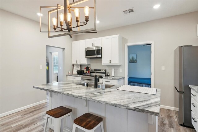 kitchen with white cabinets, appliances with stainless steel finishes, light stone countertops, light hardwood / wood-style floors, and sink