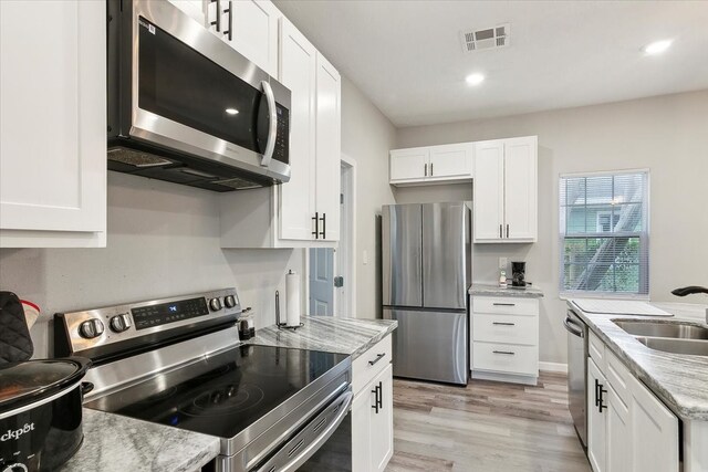 kitchen with light stone countertops, appliances with stainless steel finishes, light hardwood / wood-style flooring, and white cabinets