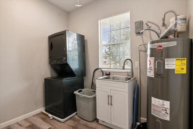 laundry area featuring stacked washer / drying machine, electric water heater, hardwood / wood-style floors, sink, and cabinets