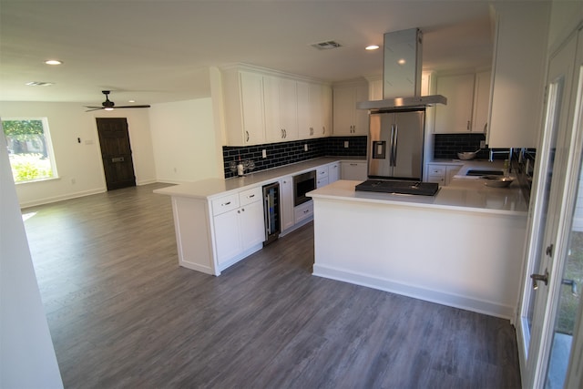 kitchen featuring kitchen peninsula, island range hood, stainless steel appliances, beverage cooler, and white cabinets