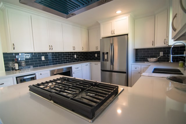 kitchen featuring backsplash, stainless steel appliances, sink, white cabinets, and wine cooler