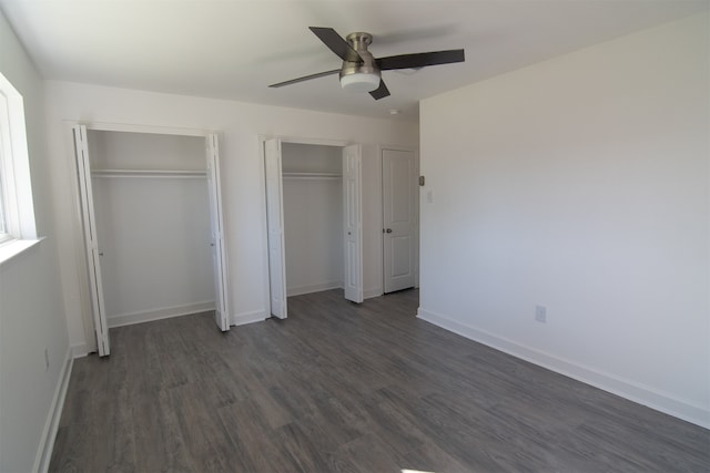 unfurnished bedroom featuring ceiling fan, dark hardwood / wood-style floors, and multiple closets