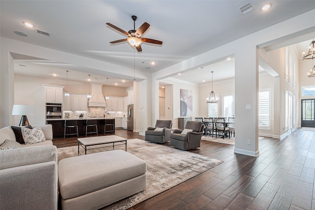 living room featuring ceiling fan with notable chandelier, a healthy amount of sunlight, dark hardwood / wood-style flooring, and crown molding