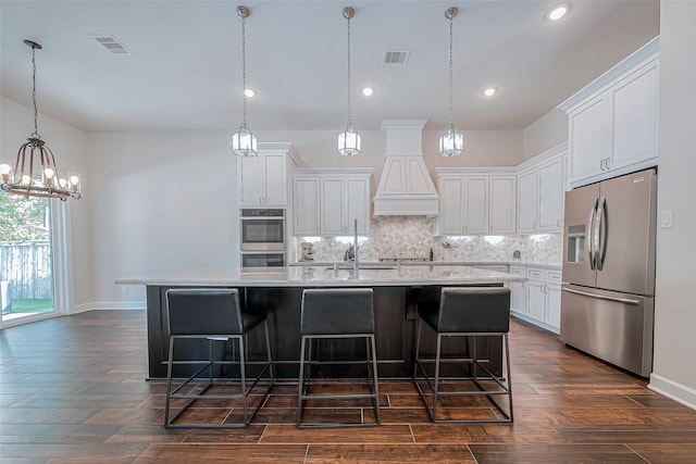 kitchen with stainless steel appliances, dark wood-type flooring, a breakfast bar area, an island with sink, and white cabinetry