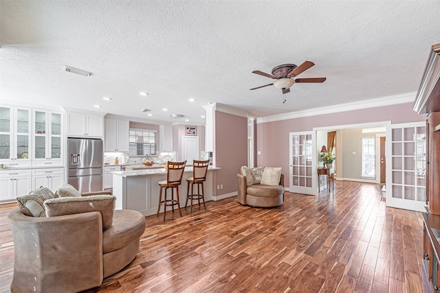 living room with a textured ceiling, wood-type flooring, ornamental molding, and french doors