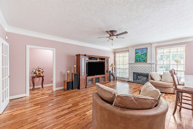 living room with ornamental molding, a textured ceiling, a tile fireplace, ceiling fan, and light hardwood / wood-style flooring