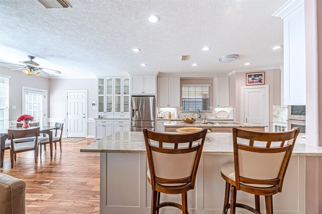 kitchen with light stone counters, stainless steel fridge, white cabinetry, a kitchen bar, and light hardwood / wood-style floors