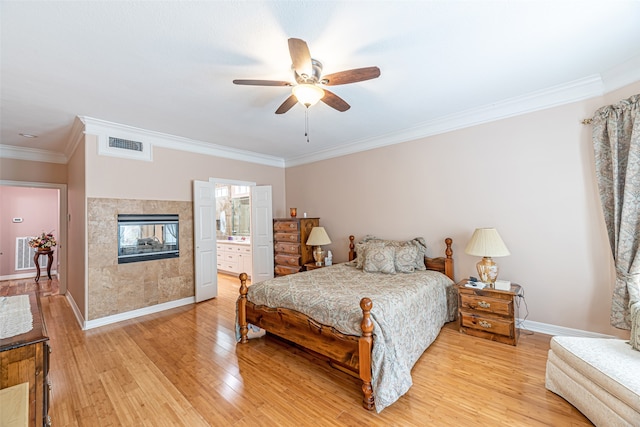 bedroom with a tiled fireplace, connected bathroom, ceiling fan, crown molding, and light hardwood / wood-style flooring