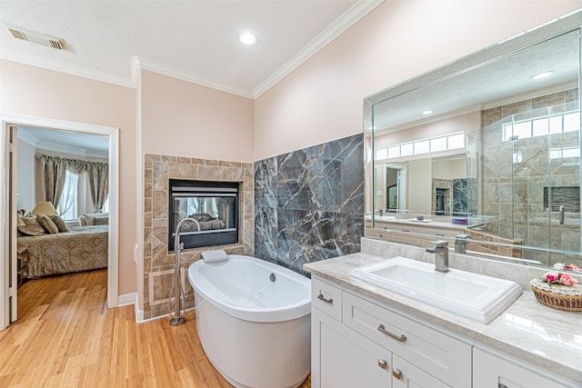 bathroom with a tiled fireplace, wood-type flooring, tile walls, ornamental molding, and vanity