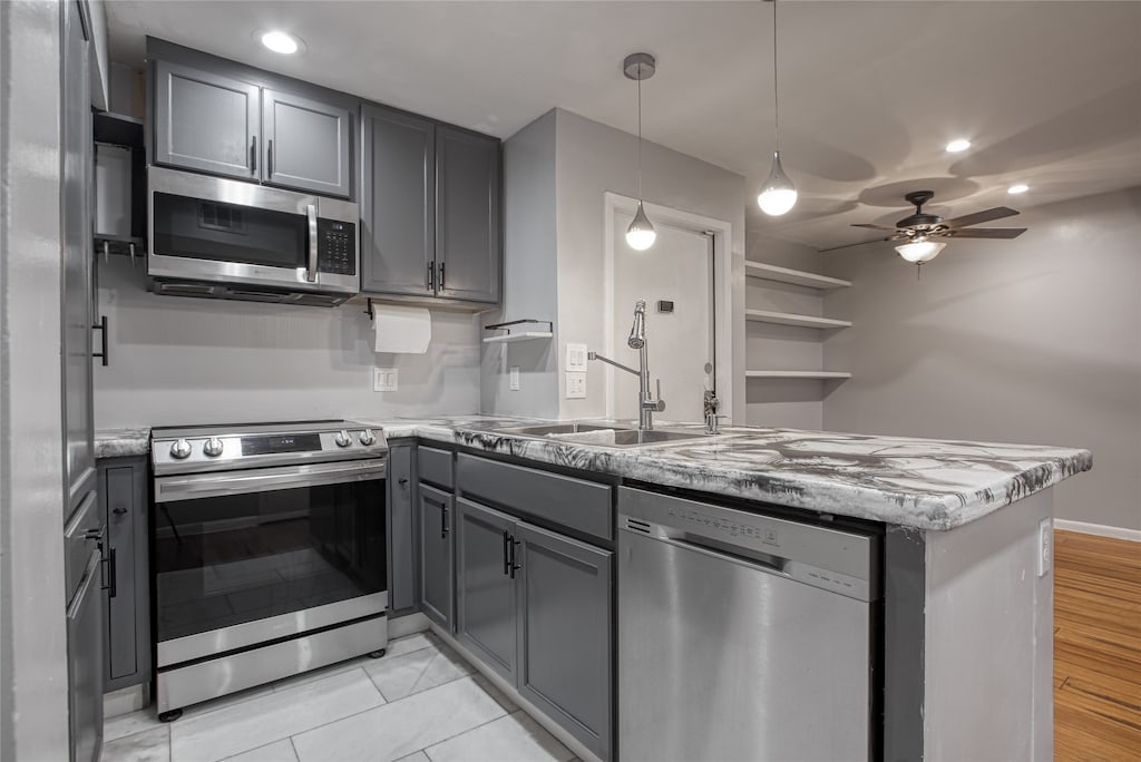 kitchen with appliances with stainless steel finishes, sink, kitchen peninsula, pendant lighting, and gray cabinets