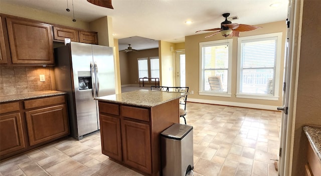 kitchen featuring backsplash, stainless steel fridge with ice dispenser, light stone countertops, a kitchen bar, and a center island