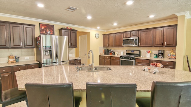 kitchen with light stone counters, a breakfast bar area, appliances with stainless steel finishes, a kitchen island with sink, and sink