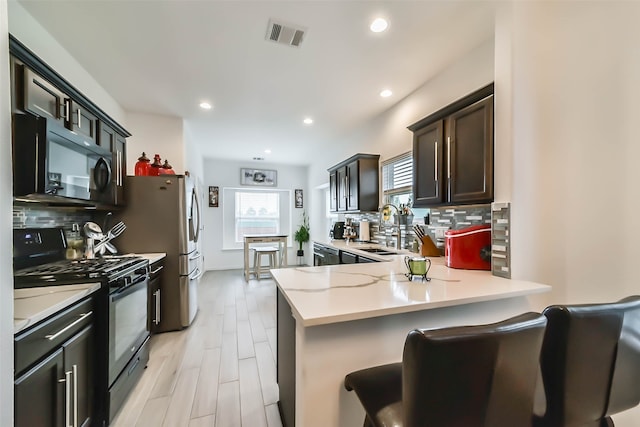 kitchen featuring black appliances, tasteful backsplash, sink, a breakfast bar, and kitchen peninsula