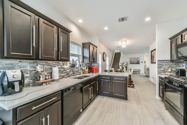 kitchen with light hardwood / wood-style floors, sink, black appliances, kitchen peninsula, and tasteful backsplash