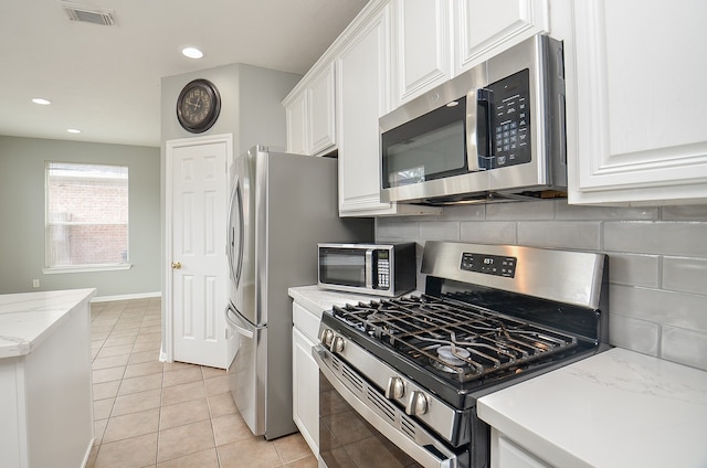 kitchen with light stone countertops, white cabinets, light tile patterned floors, and stainless steel appliances