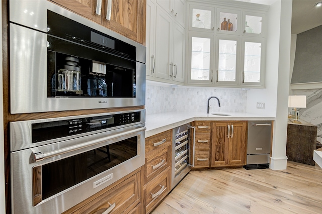 kitchen featuring beverage cooler, backsplash, white cabinetry, light hardwood / wood-style flooring, and sink