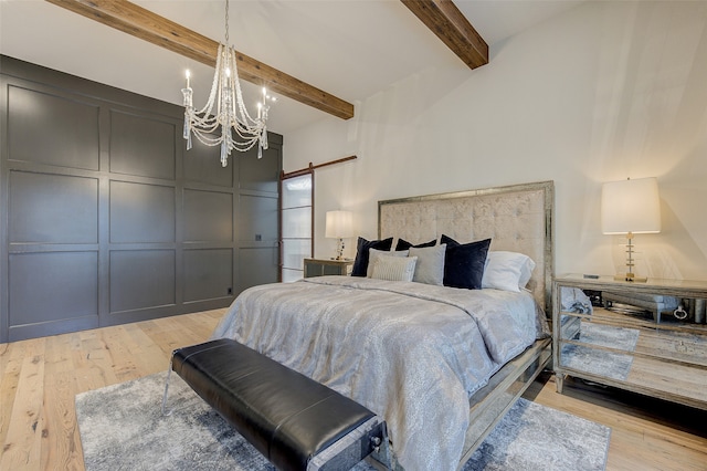 bedroom with light hardwood / wood-style floors, an inviting chandelier, a barn door, and beam ceiling