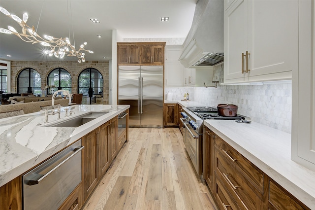 kitchen featuring wall chimney exhaust hood, light hardwood / wood-style flooring, sink, an inviting chandelier, and premium appliances