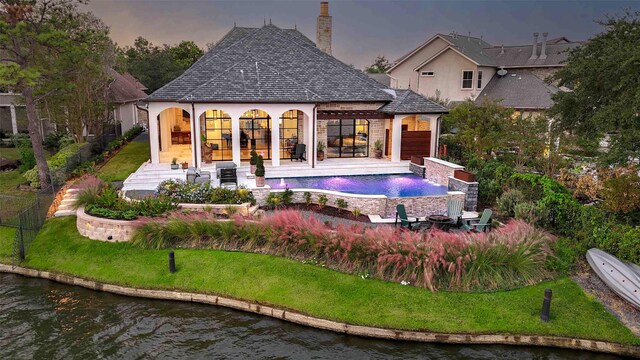 pool at dusk with a patio, pool water feature, a lawn, and a water view