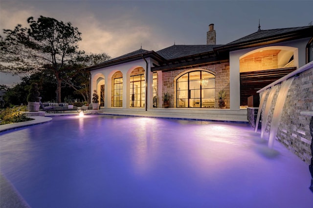 pool at dusk with a patio area and pool water feature